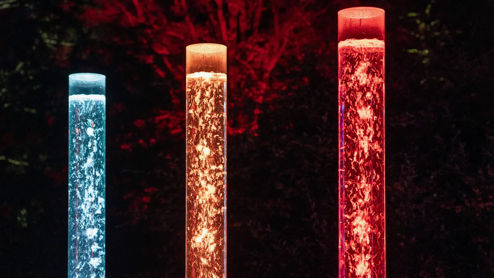Trois colonnes à bulles éclairées en rouge, bleu et orange dans une pièce sombre
